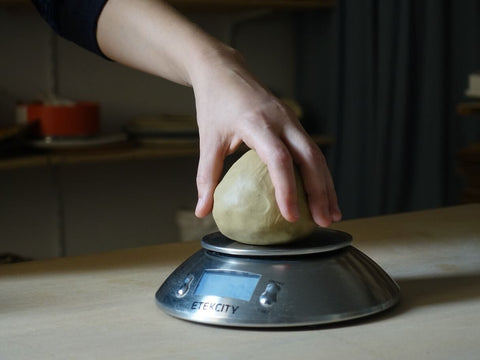 Mano che pesa un pezzo di argilla su una bilancia in uno studio di ceramica
