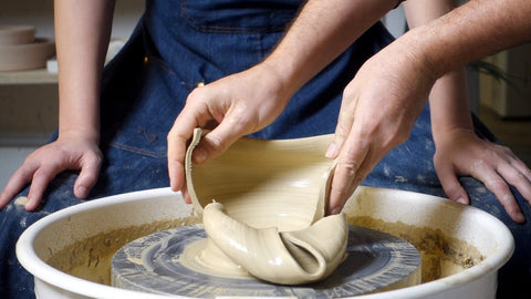Dettaglio di mani che aprono un vaso in argilla appena tornito per controllare lo spessore delle pareti